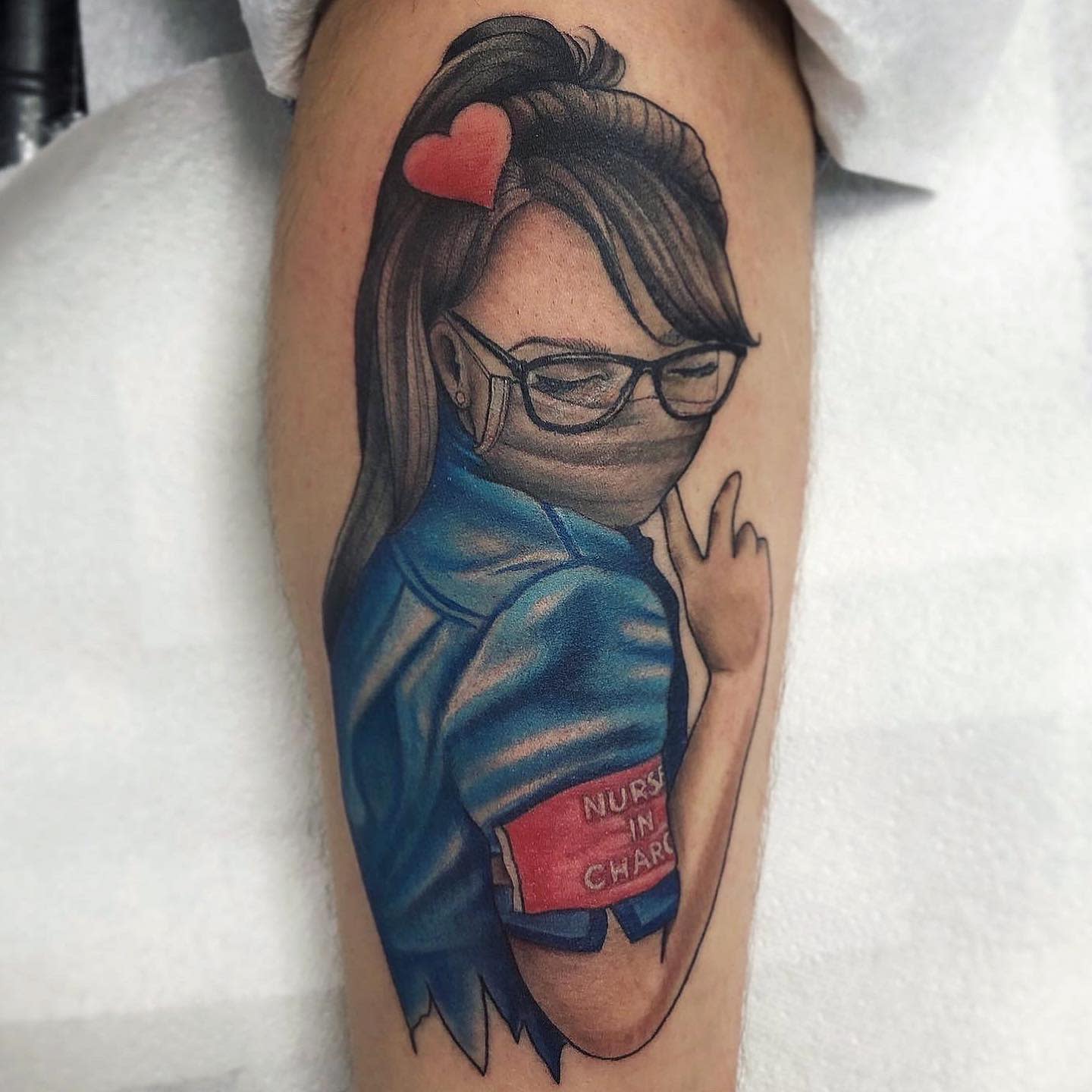 Tattoo of a nurse in blue scrubs with glasses, a mask, and a red armband